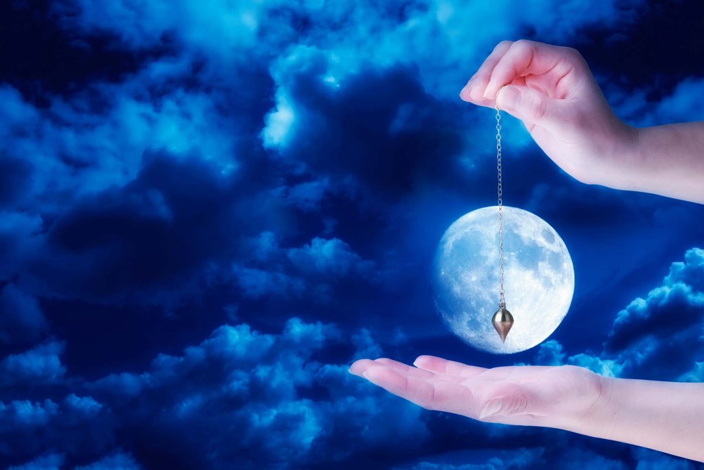 hands holding a pendulum over the image of the moon
